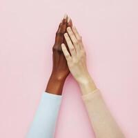 Hands of different skin tones coming together on a soft pink background signifying unity and diversity in relationships photo