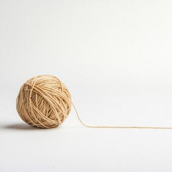 Natural yarn ball resting on a neutral background with a loose end unraveling gently photo