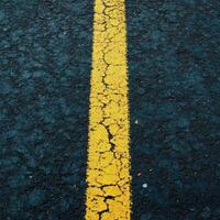 Cracked yellow line on a dark asphalt road highlighting the wear of time during daylight hours photo