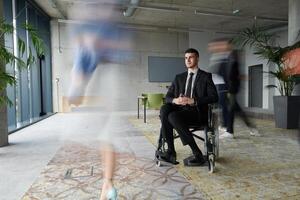 A businessman in a wheelchair navigating through a busy office, surrounded by his colleagues who are actively engaged in their work and collaboration photo