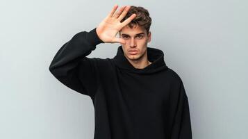 Young man in black hoodie gesturing with hand in front of blue background photo