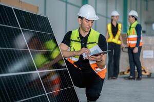 man in a yellow vest is looking at a tablet while standing next to a solar pan photo