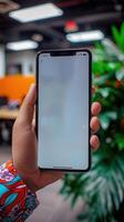 A hand holding a smartphone with a blank screen in a modern office setting photo