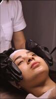 The beautician performs the procedure of microcurrents in black electric gloves to restore facial skin cells. Close-up, vertical video