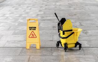Yellow warning sign with message Caution wet floor with cleaning trolley on walkway photo