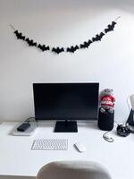 Clean and minimalistic home office desk decorated with halloween inspired black bat garland. Workspace combines functionality and seasonal charm, reflecting a balance of productivity and festivity photo