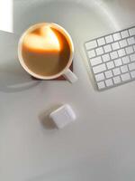 Cup of coffee with a heart-shaped reflection for Valentines day, placed on a clean white desk. Soft lighting and minimalistic workspace. Love and technologies concept. photo