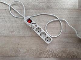 An extension cord with multiple outlets lying on a wooden floor. Practicality and utility in modern home setups. Electric power concept photo