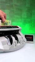 A large stack of one hundred euro bills is placed into the slot of cash counting machine. Bank equipment and financial operations. Close up. Blurred backdrop. Vertical . video
