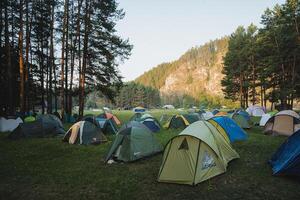 A large and diverse group of colorful tents can be seen resting peacefully on top of a vibrant, lush green field that stretches broadly across the beautiful landscape surrounding it photo