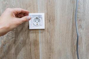 A person is skillfully plugging a cord into an electrical outlet that is located on a beautifully finished wooden wall, demonstrating a common everyday action involving electricity photo