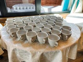 A substantial wooden table exhibits a wide range of coffee cups, each varying in size and design, resulting in an engaging and visually stunning presentation of tableware options photo