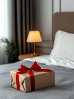 Gift wrapped in brown paper with red ribbon placed on bed in cozy bedroom photo