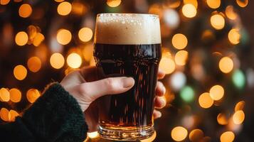 hand holding pint of stout with frothy top, festive lights in background photo