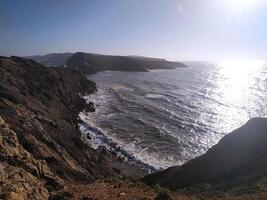 Coastal cliff view of rough waves crashing against the rocks in the afternoon sunlight at a scenic seaside location photo
