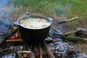 Campfire fish stew cooking in a cauldron over an open fire. photo