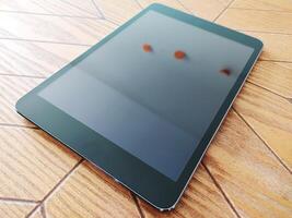 Sleek black tablet rests on a light wood table. The screen displays a blurred, out-of-focus image, creating a clean, modern aesthetic perfect for tech, business, or lifestyle projects. photo