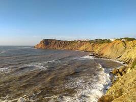 Coastal cliff view of waves crashing the rocks in the afternoon sunlight at a scenic seaside location photo