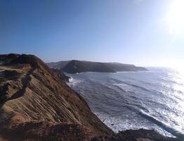 Coastal cliff view of waves against the rocks in the afternoon sunlight at a scenic seaside location photo