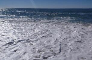 A serene beach at midday with gens lapping the shore and clear blue skies inviting relaxation photo