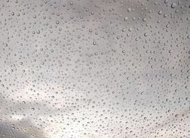 Stunning macro shot of water droplets on glass, showcasing a captivating texture against a blurred cloudy sky. Ideal for backgrounds, websites, or design projects needing a tranquil, atmospheric feel. photo