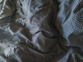 Closeup of textured dark fabric with a subtle polka dot pattern. The wrinkles and folds create a visually interesting surface ideal for backgrounds, website banners, or textile design projects. photo