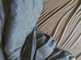 Closeup shot of a darkcolored bedsheet with a white polka dot pattern draped artfully over a solidcolored sheet. Perfect for illustrating concepts of sleep, rest, comfort, or textile design. photo