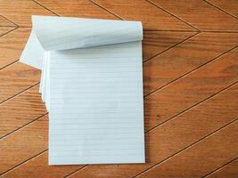 Blank lined notepad pages partially rolled, resting on a brown woodgrain surface. Perfect for showcasing your message, quotes, or product information. photo
