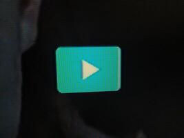 Closeup shot of a vibrant teal play button on a dark screen, showcasing the pixelated texture. Ideal for technology, media, and entertainment projects needing a modern and sleek visual. photo