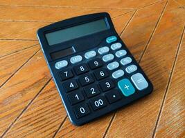 A slightly dusty, black calculator rests on a warm brown wood surface. Its simple design and clear display make it perfect for illustrating concepts of finance, math, or everyday calculations. photo