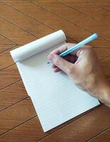 Closeup overhead shot of a hand writing on a lined notepad with a blue pen on a wood table. Perfect for concepts of notetaking, education, planning, or journaling. photo