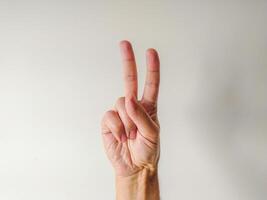 Closeup of a hand displaying the peace sign against a neutral background. Perfect for concepts of peace, unity, victory, or number two. Versatile image for websites, presentations, and social media. photo