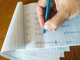 Closeup shot of a hand writing notes in a notebook with a blue pen. The lined paper shows various calculations and sketches. photo