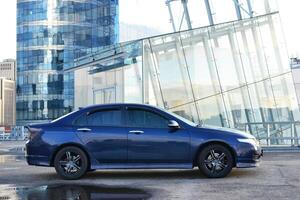 Dark blue car parked near modern glass building. photo