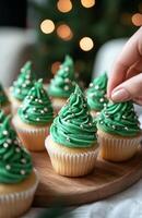 Woman hand decorating cupcakes with green frosting for Christmas trees photo