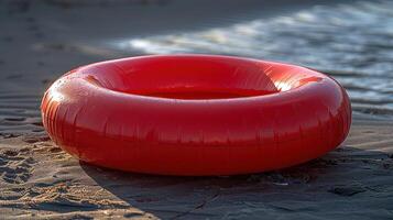 A red inflatable inner tube sits on a sandy beach, waiting for a swimmer photo