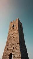 A vertical minimalist image of an ancient tower against a gradient sky is highlighted by vast negative space. photo