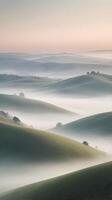 A vertical view of rolling hills blanketed in morning fog, with subdued colors and a gentle gradient sky offering space for text. photo