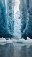 A vertical photo of a glacier's reflective face with intricate ice patterns and space for text in the blank sky above.