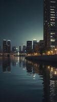 A calm vertical view of city lights shimmering on quiet water, with subdued colors and open areas for text or graphics. photo