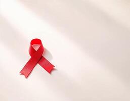 A single red ribbon lies on a light surface, representing awareness and support for various health initiatives. The soft shadows create a simple yet powerful visual statement. World Cancer Day element photo