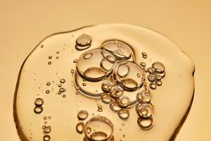 A beautiful drop of gel-like cosmetic serum with bubbles on a golden background. photo