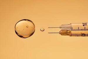 A syringe with a drop of a medical drug on a golden background. photo