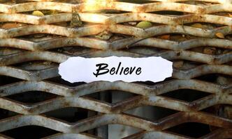 Torn piece of paper with the word believe with a background of iron fence and sunlight, words of motivation for life photo