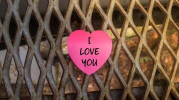 View of heart-shaped pink paper with the message I love you stuck to the iron fence. Word on paper, expressing affection and emotion for romantic concepts. photo