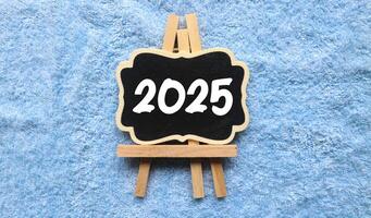 A small wooden-framed blackboard with 2025 written in white text on it. The blackboard with the concept of the new year 2025 on the blanket photo