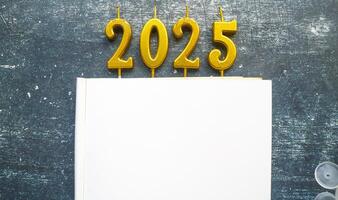 Burning golden holiday candles in shape of 2025 year on blank notebook, blank space for text. New Year 2025 celebration. photo