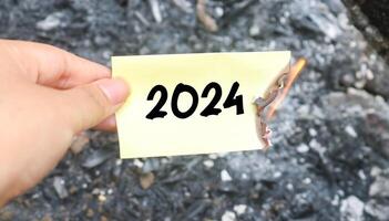 Hand holding burning paper on fire and pile of paper waste with 2024 written on it. new life and new year 2025 concept. 2024 paper is burning, say goodbye to 2024 photo