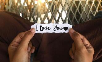 Top view of hand holding torn paper with message I love you and heart emoji. word on paper, expressing affection and emotion for romantic concepts. photo