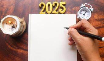candles in shape of 2025 year on blank notebook, hand writing notes on blank paper, blank space for text. New Year 2025 celebration. photo